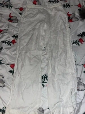 Vita vida linnebyxor med resårmidja - Säljer ett par vita linnebyxor med avslappnad passform och resår i midjan. Byxorna har raka ben och är tillverkade i ett lätt och luftigt linnematerial, perfekta för en chill och stilren look.