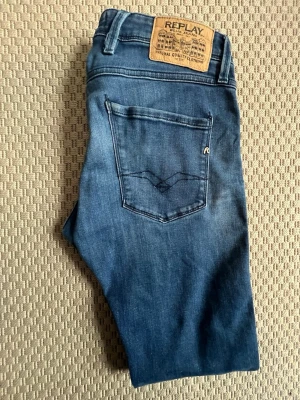 Blå jeans från Replay - Säljer ett par klassiska blå jeans från Replay med fem fickor och snygga detaljer på bakfickan. Jeansen har normal passform och är tillverkade i mjukt denimtyg med lätt tvättad look. Perfekta för dig som gillar stilrena och tidlösa jeans. W30 L32