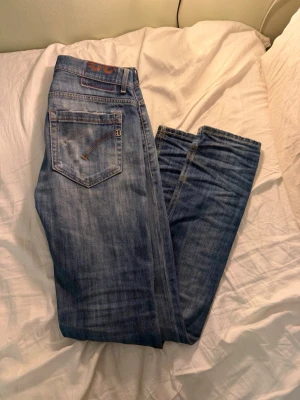 dondup Jeans - Säljer ett par klassiska blå jeans från dondup Jeans med snyggt slitna detaljer och raka ben. Jeansen har fem fickor, orange sömmar och är gjorda i mjuk denim. Perfekta för dig som gillar en avslappnad och tidlös stil. Storleken är w32 men sitter som 28-29