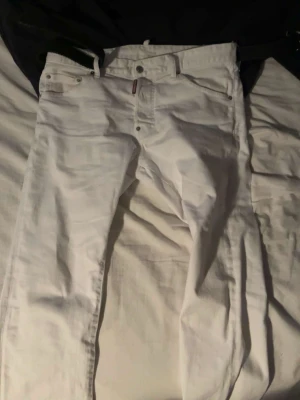 Vita jeans från Dsquared 2 - Säljer ett par vita jeans från dsq med Jeansen har bälteshällor, knappgylf och en snygg patch med logga i midjan bak. Perfekta för dig som vill sticka ut med en clean och fräsch look.