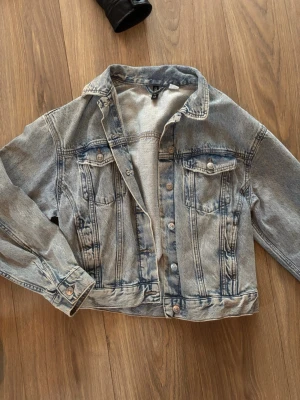 Oversized ljusblå jeansjacka - Snygg oversized jeansjacka i ljusblå tvätt med klassisk krage och knappstängning framtill. Två bröstfickor med lock och knappar samt detaljerade sömmar för en cool vintagekänsla. Perfekt att slänga över en hoodie eller t-shirt för en avslappnad look.