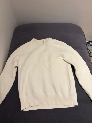 Vit stickad tröja från Uniqlo - Klassisk vit stickad tröja från Uniqlo med rund halsringning och ribbade muddar vid ärmslut och nederkant. Enkel och stilren design som passar till det mesta. Tillverkad i mjukt material för en bekväm känsla.