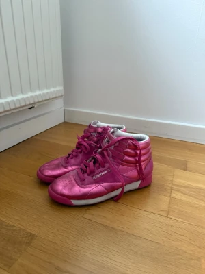 Rosa Reebok sneakers Limited edition - Säljer ett par snygga rosa sneakers från Reebok i metallicfinish. Skorna har högt skaft, vita detaljer och klassisk Reebok-logga på sidan. De har snörning och en vit sula som kontrast till det rosa. Skorna var limited edition så finns inte att få tag i idag så det är en unik chans. Väldigt bekväma! 