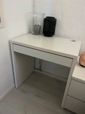 Sminkbord  - Säljer ett stilrent vitt skrivbord i enkel design med ett praktiskt kabelhål i hörnet. Bordet har raka linjer och passar perfekt för studier eller hemmakontor. Tillverkat i trä eller träkomposit med slät yta.