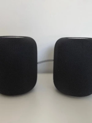 Apple HomePod par svart - Säljer ett par Apple HomePod trådlösa högtalare i svart. De har en rundad, kompakt form och är täckta av ett stilrent mesh-tyg. Perfekt för att streama musik och styra smarta hemmet med röststyrning. Snygg design som smälter in i alla rum.