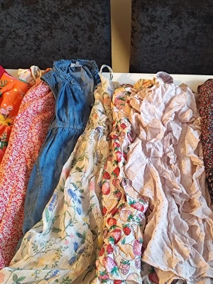 Mix av färgglada sommarklänningar 122/128 - Säljer ett gäng sommarklänningar i olika färger och mönster, bland annat blommigt, prickigt, jeans och fruktmotiv. Klänningarna är i material som bomull, jeans och polyester. Färgerna varierar från blått, rött, gult, orange till beige och vitt. Perfekta för dig som gillar unika prints och volanger.Du är varmt välkommen att kika på mina andra annonser. Sammanfrakt