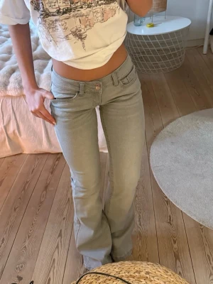 Ljusgrå lågmidjade bootcut jeans - Säljer ett par ljusgrå bootcut jeans med snygg passform och dekorativ söm på bakfickan. Jeansen har klassisk femficksdesign och är tillverkade i stretchigt denimtyg för extra komfort. Storlek S från Din Vintage Shop. Nypris: 710kr 