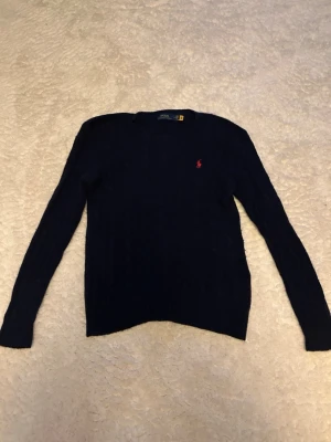 Mörkblå stickad tröja från Polo Ralph Lauren - Klassisk mörkblå stickad tröja från Polo Ralph Lauren med rund halsringning och den ikoniska röda logotypen broderad på bröstet. Tröjan har långa ärmar och ribbade muddar vid ärmslut och nederkant. Perfekt för lager på lager och stilren vardagslook. 10 procent kashmir och 90 procent merino ull. Tröjan är M i dam men passar killar som har runt xs och s. Hör av er vid funderingar.😀😀😀🔥🔥🔥🙌🙌🙌 