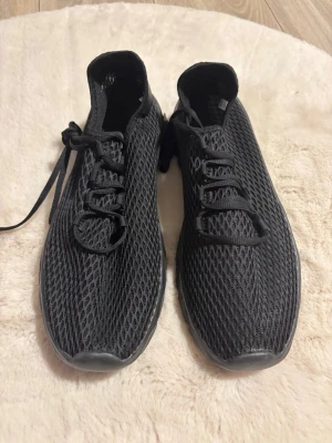 Svarta mesh sneakers med snörning - Säljer ett par helt nya helsvarta sneakers med mesh-överdel och snörning. Skorna har en låg profil och en flexibel sula som ger en sportig känsla. Perfekta för dig som gillar stilrena och lätta skor. Märke saknas.