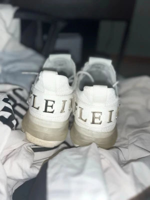 Vita sneakers från Philipp Plein  - Begagnade snygga vita sneakers från Philipp Plein med tydlig logga bak och metallmärke på plösen. Skorna har en stickad ovandel i mesh, vita snören med branding och chunky sula i beige. Perfekta för dig som vill sticka ut med exklusiv streetstyle. Begagnade som sagt lite smutsigt i framdelen. Vi kan diskutera om priset!!! Stockholm 