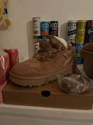 UGG LOWMEL CHESTNUT - Säljer ett par oanvända UGG Lowmel sneakers i mocka med grov sula och fluffigt foder. Skorna är helt sprillans och har inte använts pga fel storlek och för långsam retur😅 Skorna har mönstrade snören och detaljer i beige samt UGG-logga på hälen, extra helfärgade snören ingår. Perfekta för dig som vill ha både stil och komfort i vinter och vår. Priset är inte huggit i sten, som sagt är de helt nya
