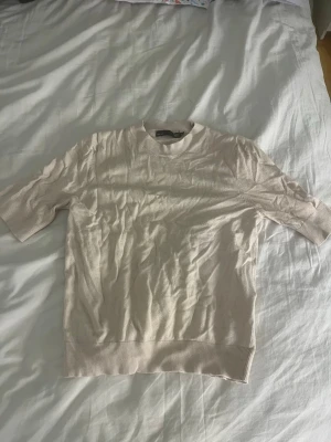 Beige ribbad topp med kort ärm - En stilren beige topp med ribbade detaljer i nederkant och hals. Toppen har korta ärmar och en klassisk rund halsringning. Perfekt för en enkel och clean look.