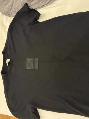 Svart Burberry t-shirt med patch - Snygg svart t-shirt från Burberry med två svarta patchar på bröstet, varav en med Burberry-loggan och riddarmotiv. Klassisk rund halsringning och korta ärmar. Tillverkad i mjuk bomull för en skön känsla och stilren look.