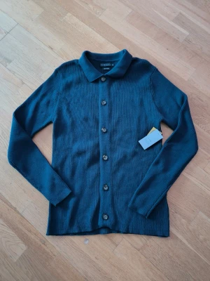 Mörkblå kofta  - Snygg mörkblå kofta  med klassisk krage och knäppning framtill. Långärmad och i mjukt stickat material, perfekt för lager-på-lager. Enkel och stilren design som passar till det mesta.