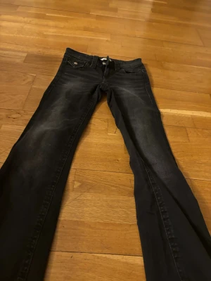 Svarta bootcut jeans med slitningar - Säljer ett par svarta bootcut jeans med snygga slitningar på låren. Jeansen har klassisk femficksdesign och knappgylf. Materialet är troligtvis bomull med lite stretch för skön passform. Perfekta för en avslappnad och trendig look.