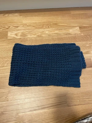 Mörkblå stickad halsduk - En chunky, mörkblå stickad halsduk med grovt mönster. Perfekt för att hålla värmen under kyliga dagar. Halsduken är rektangulär och har breda ribbade kanter. 