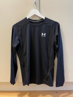 Svart långärmad compression-tröja Under Armour - Säljer en svart långärmad träningströja från Under Armour. Tröjan har en tight passform, rund halsringning och är tillverkad i ett stretchigt funktionsmaterial som transporterar bort fukt. Perfekt för gym eller löpning.
