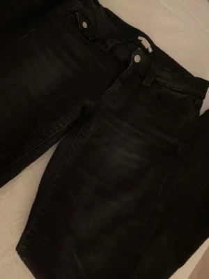 Svarta jeans med fickdetaljer - Säljer ett par svarta jeans med bootcut och snygga fickdetaljer både fram och bak. Jeansen har silverfärgade knappar och bälteshällor. Perfekta till en avslappnad streetstyle-look. Materialet är klassisk denim i bomull.