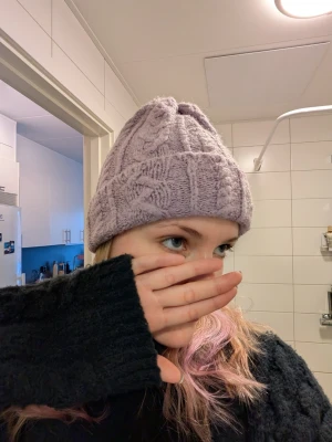 Ljuslila kabelstickad mössa - Säljer en mysig ljuslila mössa med kabelstickat mönster och uppvikt kant. Mössan är tillverkad i mjukt garn och har en klassisk form som passar perfekt för kalla dagar. Perfekt accessoar för att hålla värmen och samtidigt se snygg ut.