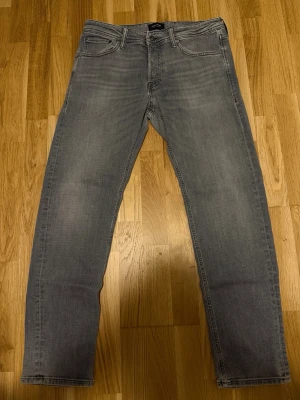 Grå raka jeans från Jack and Jones  - Snygga grå jeans med rak passform och klassisk femficksdesign. Jeansen har diskreta slitningar och en stilren look som passar till det mesta. Tillverkade i mjukt denimtyg för en bekväm känsla hela dagen.