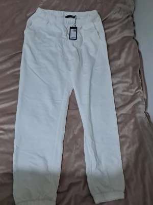 Julie Vita mjukisbyxor från lager 157 - Säljer ett par vita mjukisbyxor från lager 157 "Julie" med resår i midjan och vid bensluten. Byxorna har en avslappnad passform och är tillverkade i mjukt material som passar perfekt för chill dagar. Klassisk design utan synliga loggor eller tryck. Orginal 150kr mitt pris 49kr