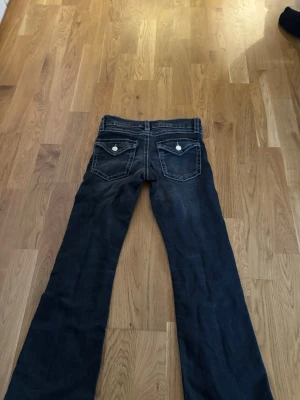 Bootcut jeans med kontrastsömmar - Säljer ett par mörkblå bootcut jeans med vita kontrastsömmar och två bakfickor med lock och knappdetaljer. Jeansen har låg midja och klassisk femficksdesign. Perfekta för en avslappnad och trendig look.