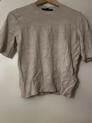 Beige stickad topp från lager  - Beige stickad topp från lager med rund halsringning och korta ärmar. 