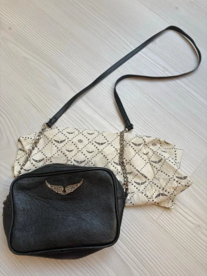Svart axelväska från Zadig & Voltaire🖤 - Snygg svart axelväska i läder från Zadig & Voltaire med silverfärgad kedja och ikonisk vingdetalj framtill. Väskan har en rektangulär form och justerbar axelrem. Perfekta väskan som är så användbar 🫶🏼
