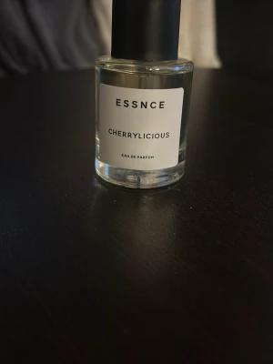 ESSNCE Cherrylicious Eau de Parfum - Fräsch parfym från ESSNCE med doften Cherrylicious. Kommer i en stilren, genomskinlig glasflaska med svart lock och vit etikett. Perfekt för dig som gillar fruktiga och söta dofter.