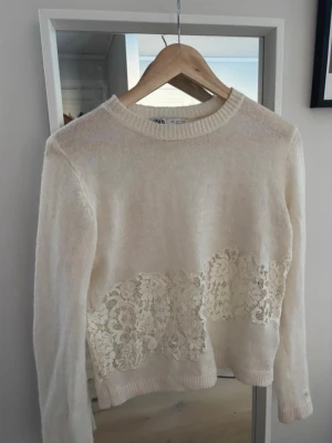 Vit stickad tröja med spets från ZARA - Säljer en söt vit stickad tröja från ZARA. Tröjan har spetsdetalj runt midjan både fram och bak. Tröjan har använts 1-2 gånger och är storlek S