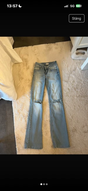 Lågmidjade jeans - Säljer ett par ljusblå jeans från Nelly med raka ben och slitningar över knäna, stolen 34. Lite nedtrampad längst ner annars super fina!❤️