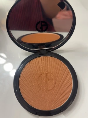 Giorgio Armani solpuder bronzer - Snygg bronzer från Giorgio Armani i en varm, gyllenbrun nyans med subtilt skimmer. Kommer i en rund, elegant dosa med spegel och GA-logga på locket. Perfekt för att ge ansiktet en solkysst look och highlighta kindbenen. Endast använd en gång och säljer pågrund av fel shade