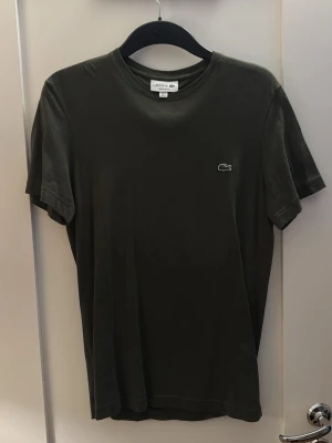 Mörkgrön Lacoste t-shirt i bomull - Snygg mörkgrön t-shirt från Lacoste med klassisk krokodillogga på bröstet. Tillverkad i mjuk bomull och har en enkel, stilren design med rund hals och korta ärmar. Perfekt för en clean och avslappnad look.