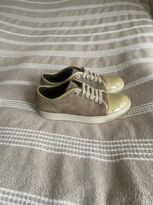 Lanvin Beige sneakers med lackad tå - Snygga beige sneakers med mockaliknande material på sidorna och glansig, ljusgul lackad tå och häl. Skorna har vita snören och vit sula. Perfekta för dig som gillar en clean och stilren look med en twist.