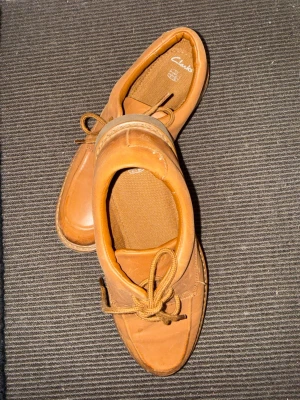 Bruna loafers från Clarks i läder - Säljer ett par klassiska bruna loafers från Clarks i mjukt läder. Skorna har rundad tå, snörning framtill och en rejäl räfflad gummisula för extra grepp. Perfekta för dig som gillar tidlös stil och vill ha något bekvämt till vardagslooken.