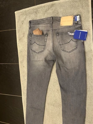 Grå skinny jeans från Jacob cohen - Säljer ett par grå skinny jeans från Jacob cohen med snygga slitningar och klassisk femficksdesign. Jeansen har blå detaljer vid fickorna och är tillverkade i stretchigt bomullsmaterial för en bekväm passform. Helt nya modell : bard. Og tillkommer och pris kan diskuteras 
