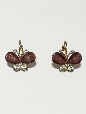 Lilarosa fjärilsörhängen med stenar - Snygga örhängen i form av fjärilar med lila / rosa pärlliknande vingar och glittrande stenar i botten. Örhängena har guldfärgade detaljer och en smidig krok för enkel användning. Perfekt accessoar för att lyfta din stil med en söt och trendig touch. Helt NYA i förpackning. 