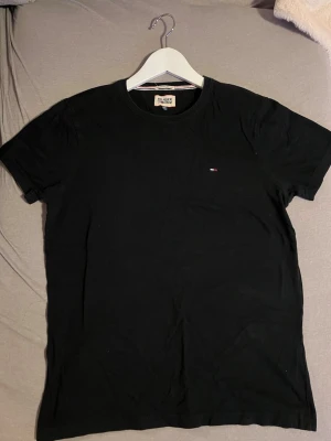 Svart t-shirt från Hilfiger Denim - Klassisk svart t-shirt från Hilfiger Denim med liten broderad logga på bröstet. T-shirten har rund halsringning och korta ärmar. Tillverkad i mjuk bomull för en skön känsla och enkel stil.