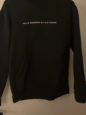 Svart hoodie från Boostat med tryck - Svart hoodie från Boostat med vit text 'HELLO DARKNESS MY OLD FRIEND' på bröstet. Klassisk modell med huva, snörning och magficka. Perfekt för en chill och avslappnad stil.