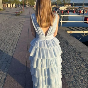 Ljusblå långklänning med volanger från bubbelroom - Säljer en drömmig ljusblå långklänning med djup v-ringning och öppen rygg från bubbelroom.  Perfekt för bal eller fest! Jag är 165 och är i bra längd för mig med klackskor. Använd 2 gånger 