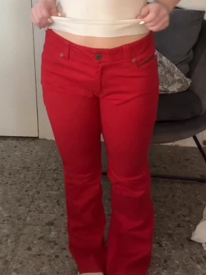 Röda bootcut jeans med låg midja - Otroligt snygga röda lågmidjade bootcut jeans. Klassisk femficksmodell med knapp och dragkedja framtill. Perfekta för dig som vill sticka ut med färg och gillar en lite coolare stil.