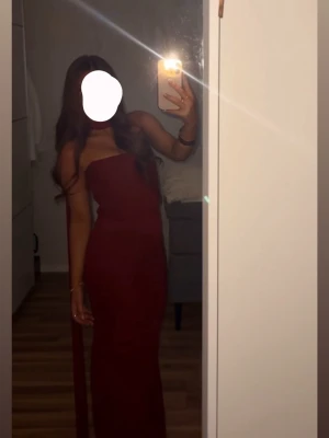 Vinröd axelbandslös långklänning - Säljer en elegant vinröd långklänning med axelbandslös design och figurnära passform. Klänningen har en stilren look och är perfekt för speciella tillfällen. Materialet känns mjukt och följsamt mot kroppen.