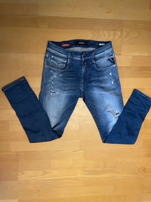 Replay jeans   - Säljer ett par blå skinny jeans från Replay med slitningar och lätt tvättad look. Jeansen har fem fickor, dragkedja och knapp i midjan samt Replay-logga på fickan. Perfekta för en avslappnad och trendig stil.