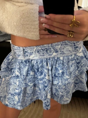 Blåvit volangkjol med blommönster - supersöt mönstrad kjol i vit och blå! Perfekt till sommaren och passar till det mesta🩵kjolen är i storlek xxs men är strechig och kan då passa xs och s också💫 aldrig använt! 