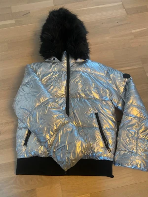 Silvrig pufferjacka med pälsluva - Priset kan diskuteras!!! En jätte fin silvrig varm vinterjacka med avtagbar fauxpäls, köpt i London, bra skick nästan inte använd. Säljer eftersom den används inte. Är i storlek XS men passar S också.