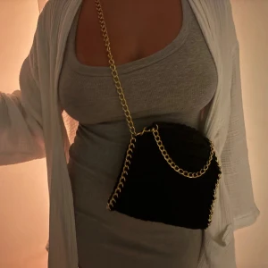 Mörk blå virkad axelväska med guldkedja - Säljer en mörkblå virkad axelväska med snygg guldfärgad kedja som axelrem. Väskan är köpt av ett gammalt Uf företag och är därför väldigt unik och går inte att köpa längre.