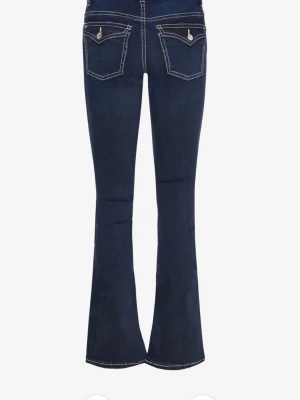 Mörkblå bootcut jeans med kontrastsömmar - Snygga mörkblå bootcut jeans med vita kontrastsömmar och klassisk femficksdesign. Jeansen har utsvängda ben och låg midja, perfekta för en trendig och avslappnad look. Tillverkade i stretchig denim för extra komfort.