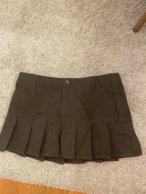 Grå brun volang kjol - Säljer en brun kortkjol med plisserad nederdel och fickor fram. Kjolen har en knapp och dragkedja i midjan och är gjord i ett stadigt bomullstyg. Perfekt för dig som gillar en sportig och trendig stil. Alldrig använd eftersom det är fel stolek för mig. 
