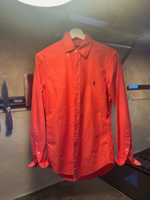 Korall skjorta från Ralph Lauren XS - Säljer en korall skjorta från Ralph Lauren i slim fit-modell. Skjortan har klassisk krage med knappar, lång ärm och den ikoniska broderade loggan på bröstet. Tillverkad i mjuk bomull och passar perfekt till en clean och stilren look.