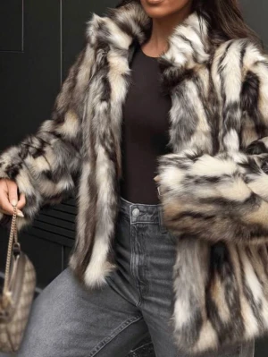 Zara Fuskpälsjacka i svart och vit - Säljer en fluffig och trendig fuskpälsjacka i svart, vit och grått med bred krage och rak passform. Jackan har ett coolt mönster och är perfekt för att hålla värmen under kalla dagar. Stängs framtill och har långa ärmar. Perfekt statement-plagg för vintern.